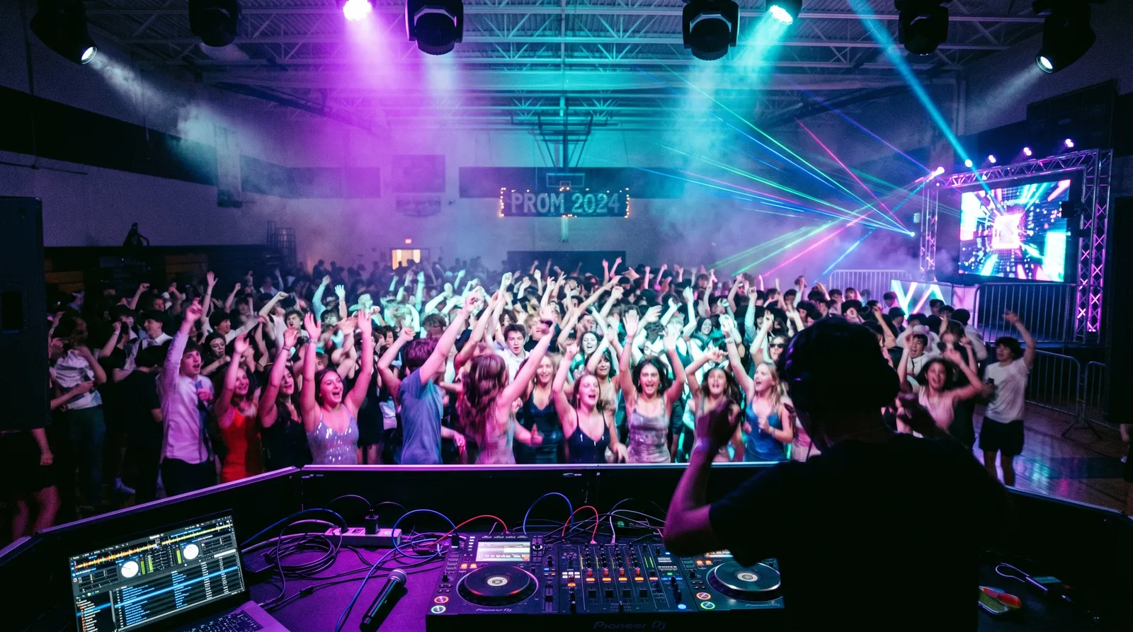 A high school prom dance floor packed with students cheering under purple and cyan stage lights